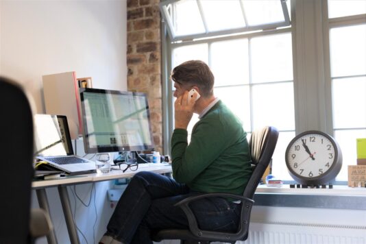 An image of a man sitting at his desk taking a client call.