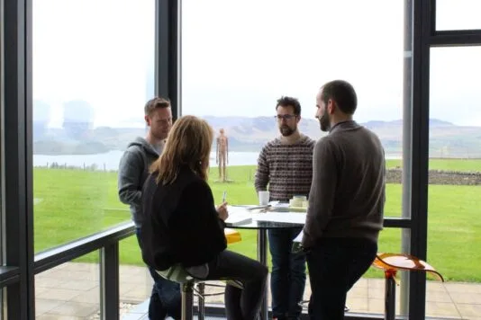 Colleagues sitting and standing around a tall table chatting to each other.