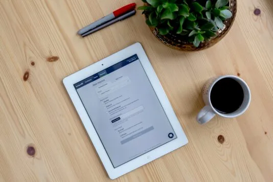 Image of the Amiqus interface being shown on a tablet sitting on a table with a cup of coffee, pens and a plant sitting around the device.