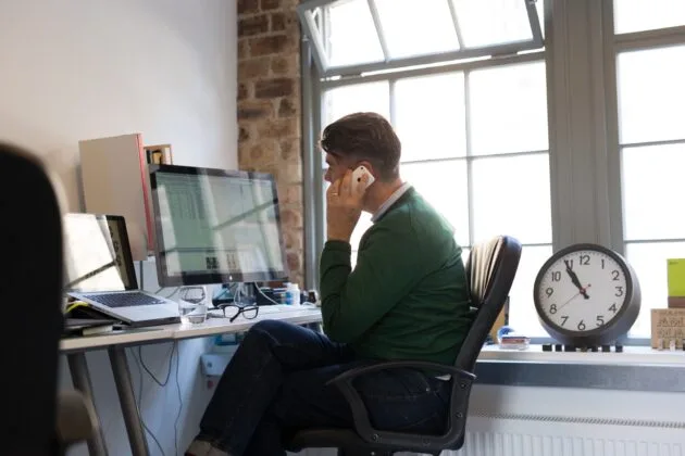 Employee working at computer while taking a call on his phone.