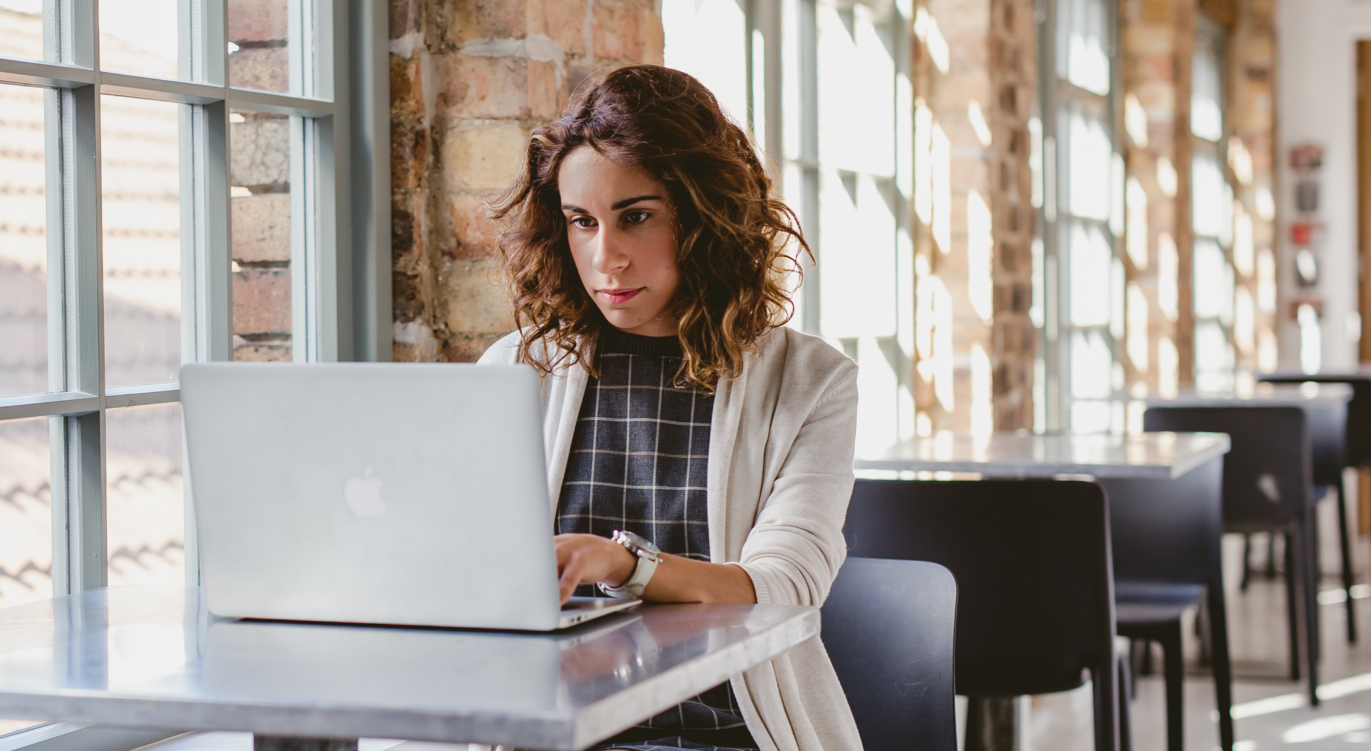 Image of a woman with curly hair working on laptop in an office. With empty desks behind her.