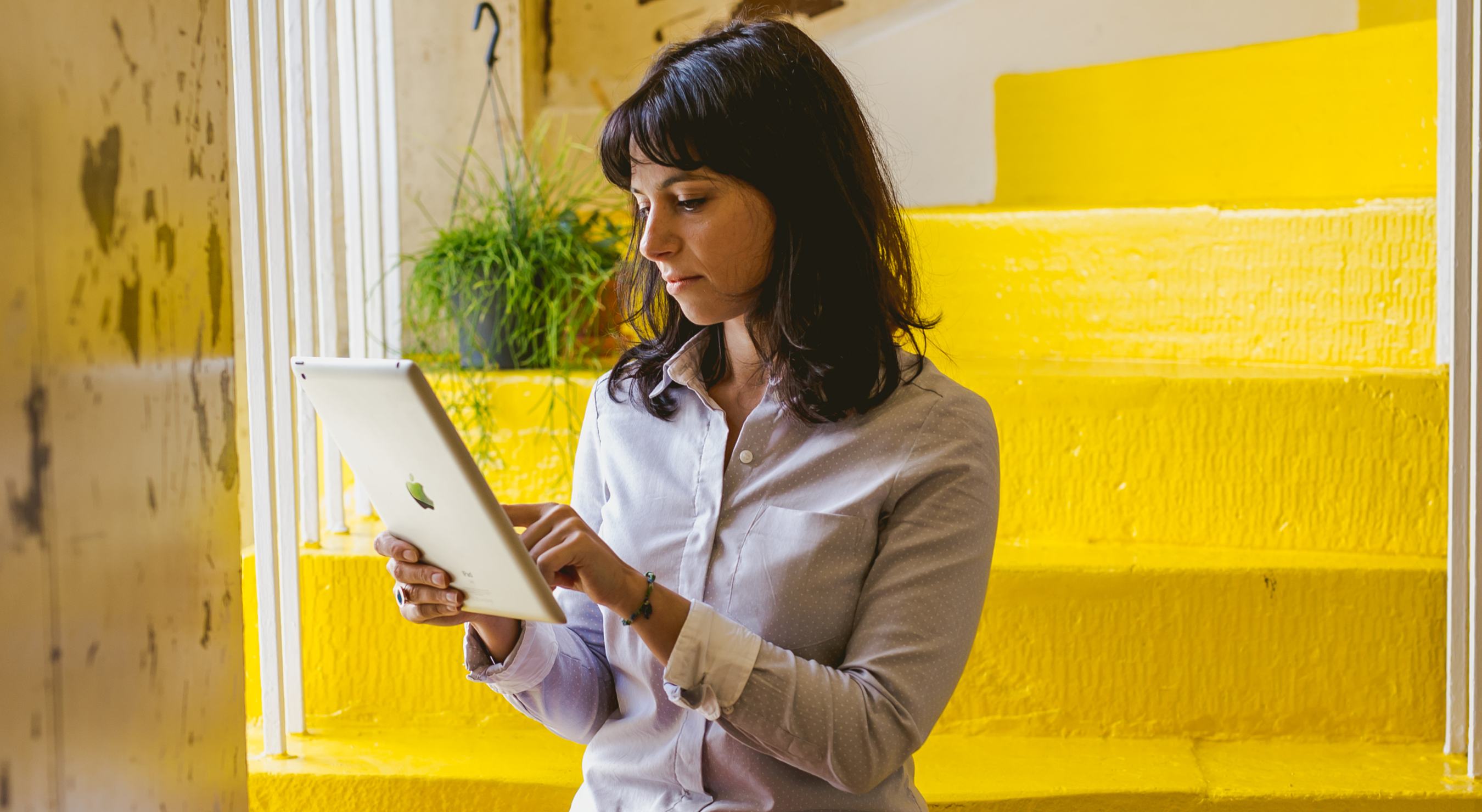 An image of woman using an iPad with yellow stairs in background.