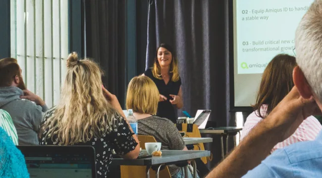 An image of the Amiqus team with a team member presenting a presentation from a projector.