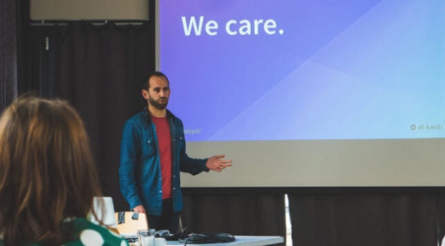 The CEO Callum Murray presenting to the Amiqus team with a slide behind him saying "We care."