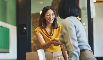 Businesswoman shaking hands with client and smiling cheerfully in meeting room